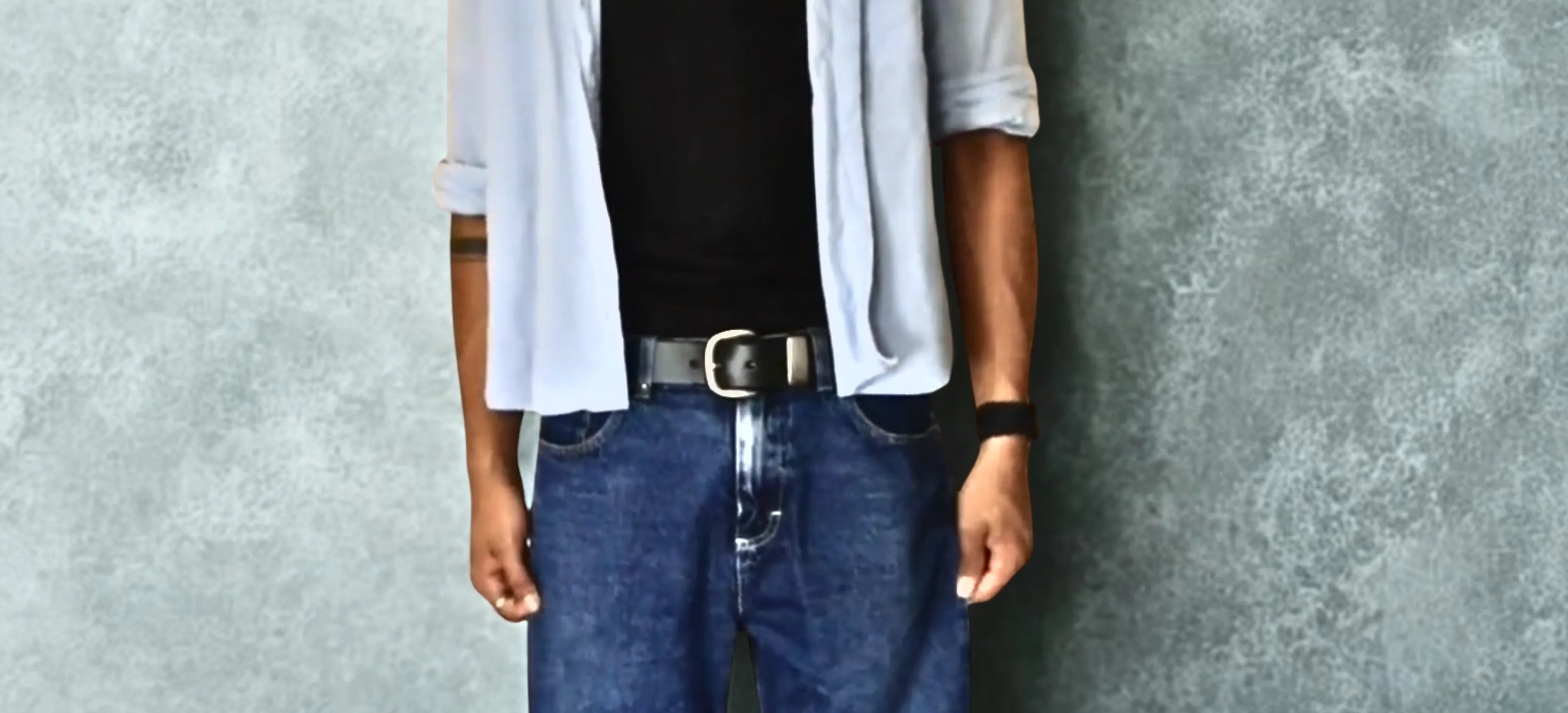 person wearing a black belt with silver buckle standing in front of a blurred background.