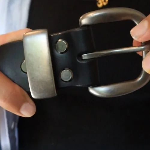 Close-up of a black belt with a silver buckle held by hands against a dark background